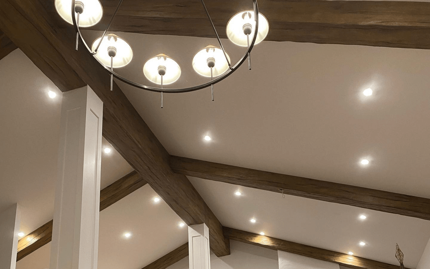 Vaulted ceiling with decorative beams, recessed downlights spaced between the bays and a pendant chandelier