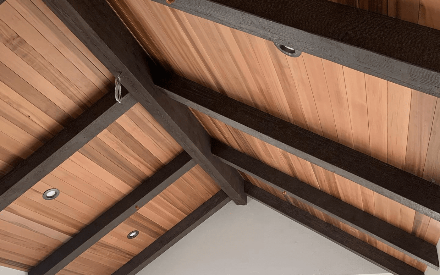 Close-up of decorative beams meeting at an intersection against a cedar plank ceiling with recessed downlights