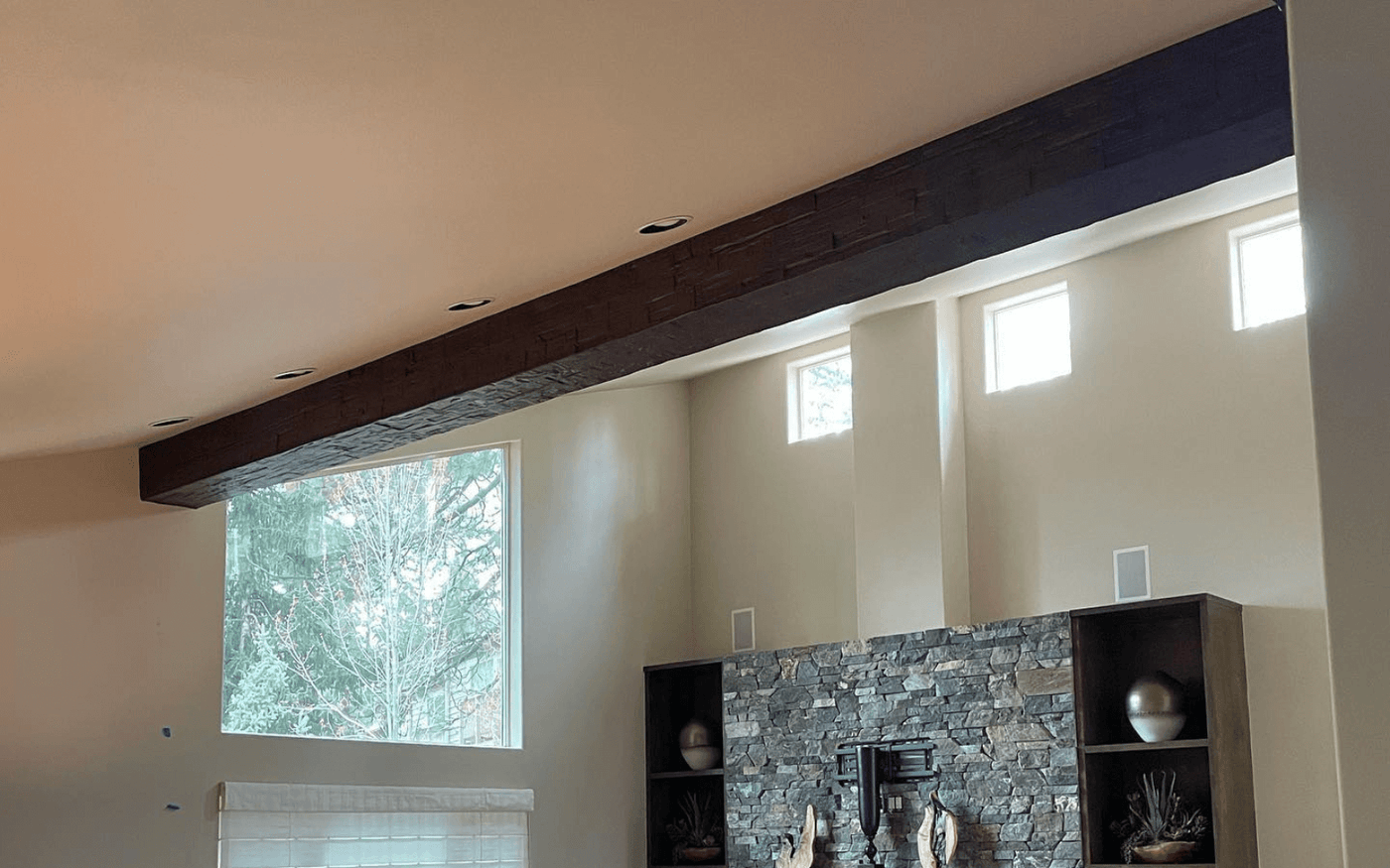 Single large decorative beam spanning a vaulted living room above a stone fireplace and stacked shelving