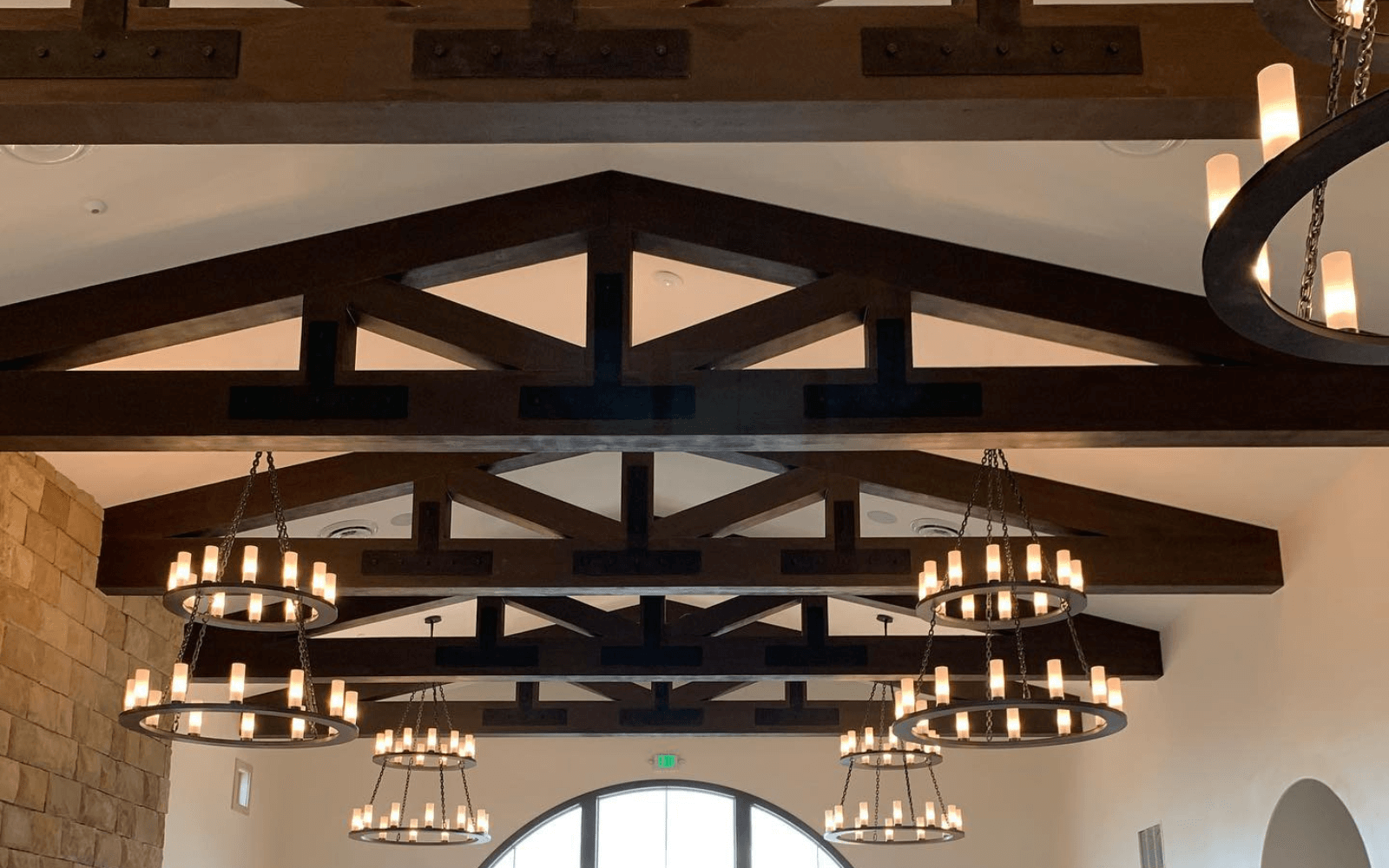 Dark stained faux trusses over an arched opening with chandeliers