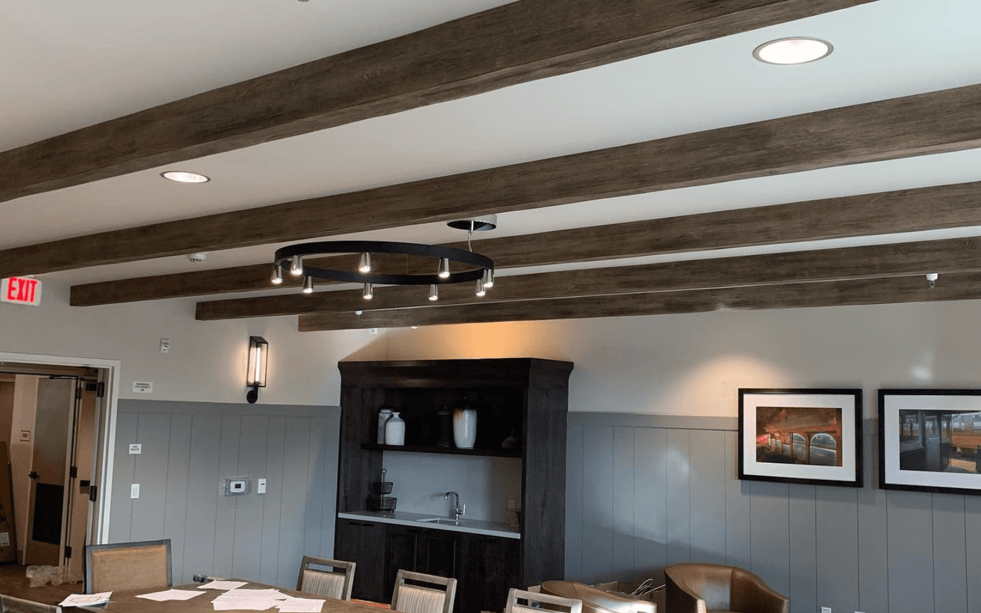 Commercial clubhouse ceiling with dark decorative beams, recessed downlights and a ring pendant fixture